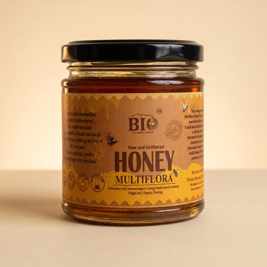 A jar of BIO Organic Honey Multiflora raw and unfiltered honey, featuring a black lid and a warm brown label, set against a solid beige background.